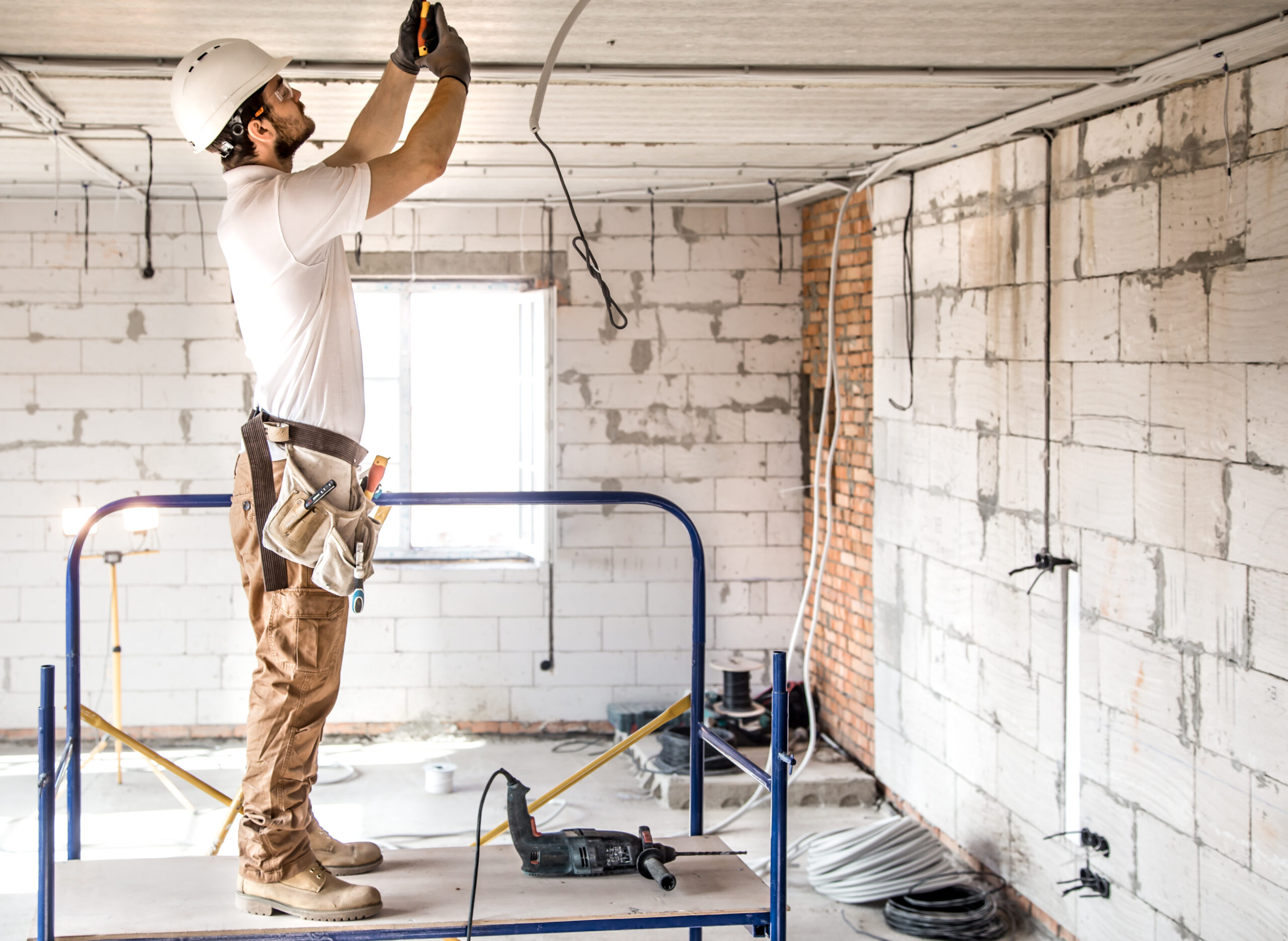 Electrician installer with a tool in his hands, working with cable on the construction site. Repair and handyman concept. House and house reconstruction.