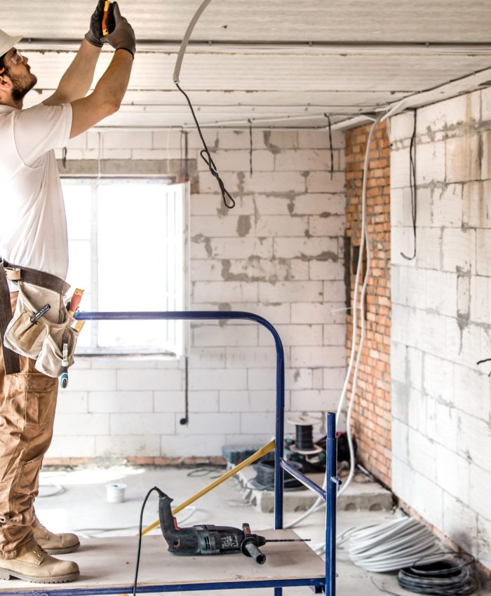 Electrician installer with a tool in his hands, working with cable on the construction site. Repair and handyman concept. House and house reconstruction.